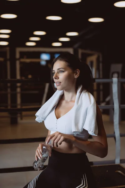 Wanita muda cantik dengan handuk di pundaknya botol air terbuka di gym — Stok Foto