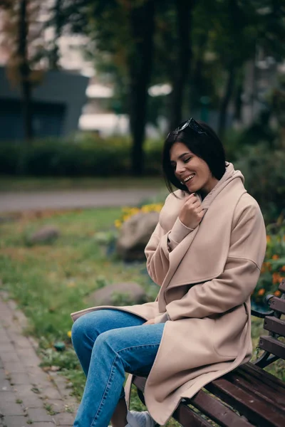 Šťastná mladá bruneta sedí na lavičce v parku — Stock fotografie