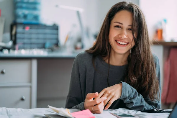 Porträt eines lächelnden süßen Hipster-Mädchens, das in die Kamera starrt, während es College-Übungen in Notizbuch schreibt. — Stockfoto