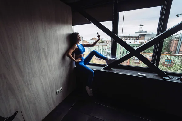 Menina bonita sentada no peitoril da janela com smartphone em mãos . — Fotografia de Stock