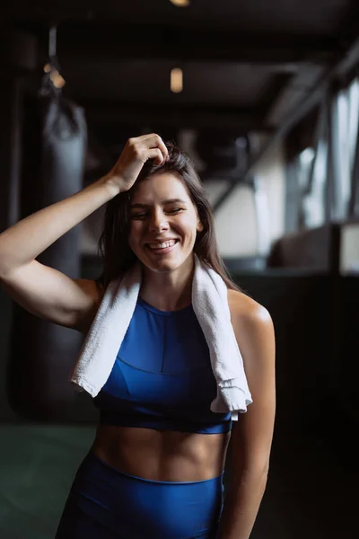 Sonriente chica en forma sosteniendo la toalla y descansando en el gimnasio . — Foto de Stock