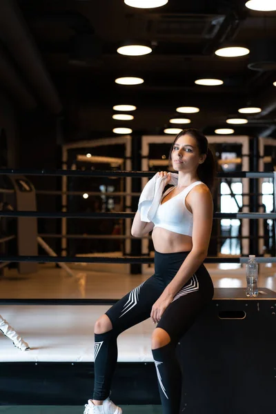 Sonriente chica en forma sosteniendo la toalla y descansando en el gimnasio . — Foto de Stock