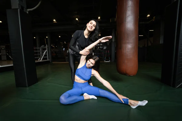 Two beautiful young girls doing fitness in a gym. Stretching the muscles of the legs and arms.