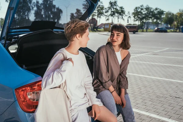 Dos chicas en el estacionamiento en el maletero abierto posando para la cámara. —  Fotos de Stock