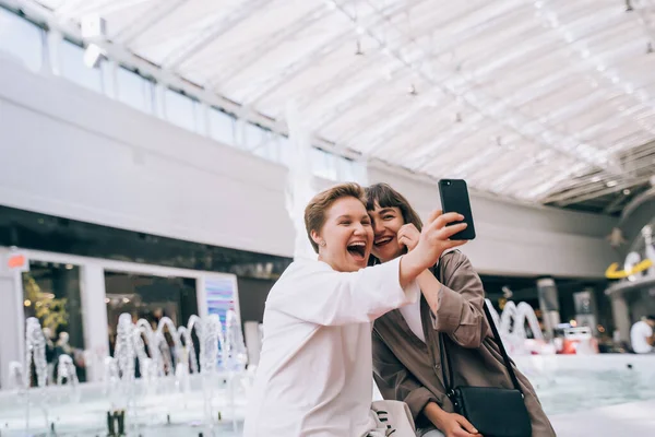 Duas garotas pegam uma selfie no shopping, uma fonte no fundo — Fotografia de Stock