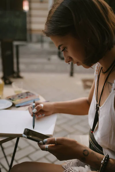 Mladá žena kreslí na skicáku s tužkou venku na ulici — Stock fotografie