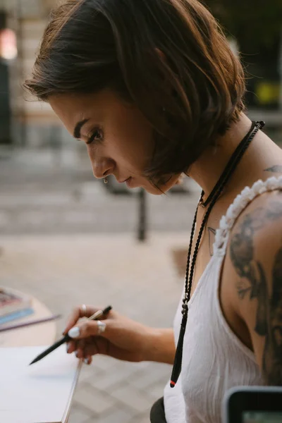 Mladá žena kreslí na skicáku s tužkou venku na ulici — Stock fotografie