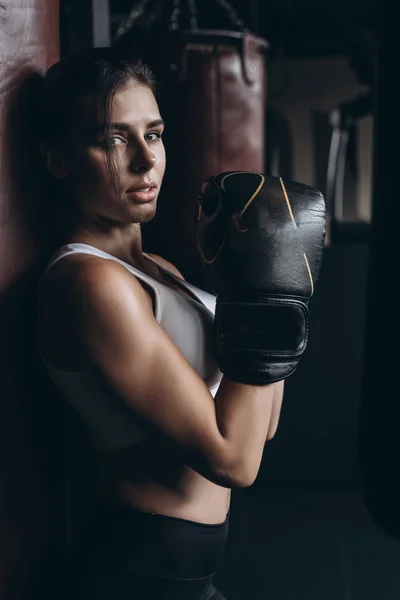 Mulher de boxe posando com saco de perfuração, em fundo escuro. Conceito de mulher forte e independente — Fotografia de Stock