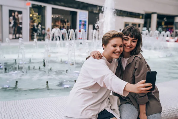 Dvě holky si berou selfie v obchoďáku, fontánu v pozadí — Stock fotografie