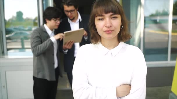 Jovem, bela mulher posando para a câmera, no fundo dois empresários — Vídeo de Stock
