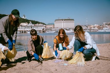 Bir grup aktivist arkadaş plajda plastik atık topluyor. Çevresel koruma.