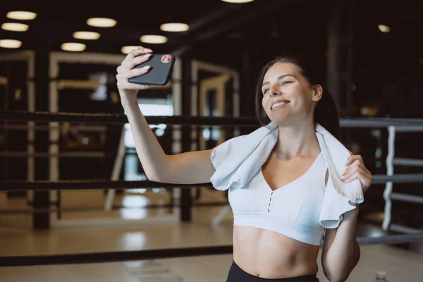 Wanita muda sporty mengambil selfie dengan ponsel untuk jejaring sosial di gym . — Stok Foto