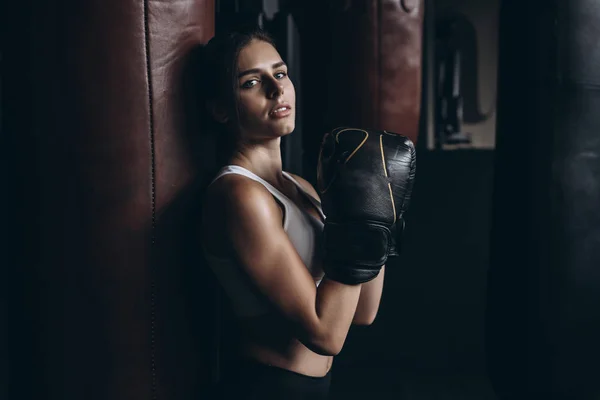 Mulher de boxe posando com saco de perfuração, em fundo escuro. Conceito de mulher forte e independente — Fotografia de Stock