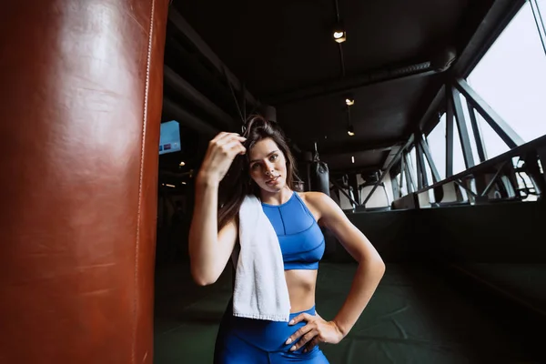 Mosolygós fitt lány gazdaság törülköző és pihenés tornaterem közelében boxzsák — Stock Fotó
