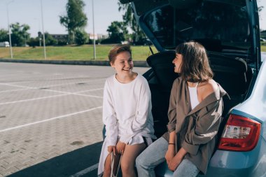 Açık bagajdaki park yerinde kameraya poz veren iki kız..