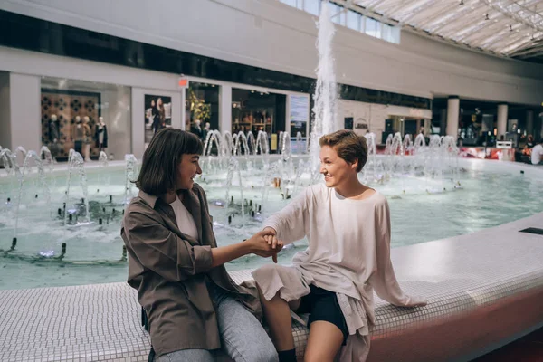 Two girls have fun in the mall, a fountain in the background — Stock Photo, Image