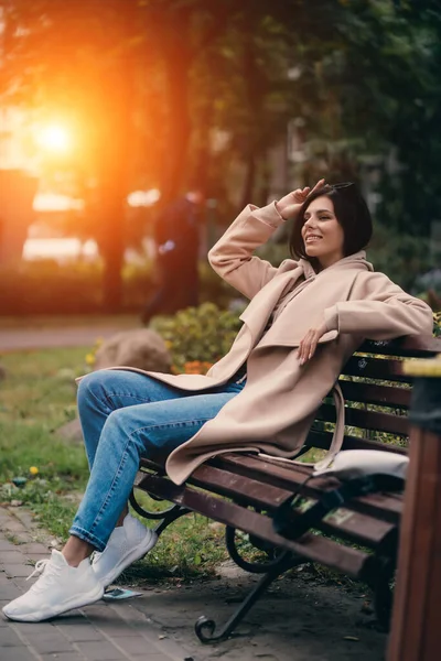 Jovem morena feliz sentada em um banco de parque — Fotografia de Stock