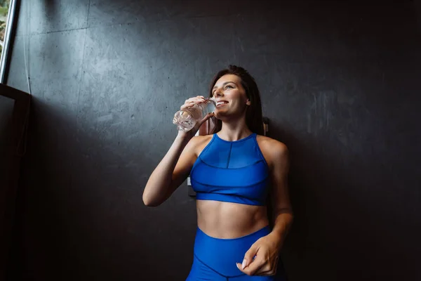 Mujer en forma posando en la cámara. La chica bebe agua de una botella. Belleza del deporte moderno . — Foto de Stock