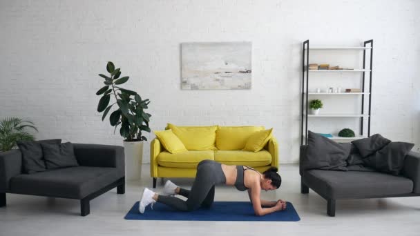 Hermosa joven hace ejercicios para el abdomen en la alfombra en la habitación — Vídeo de stock