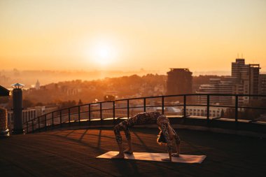 Büyük şehirde bir gökdelenin çatı üzerinde yoga yaparken kadın.