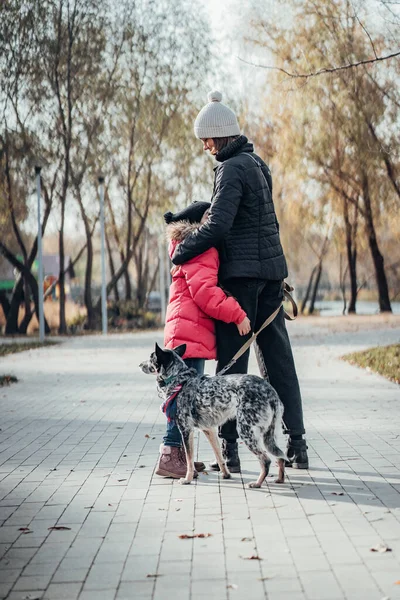 Счастливая мать и ее дочь гуляют с собакой в осеннем парке — стоковое фото
