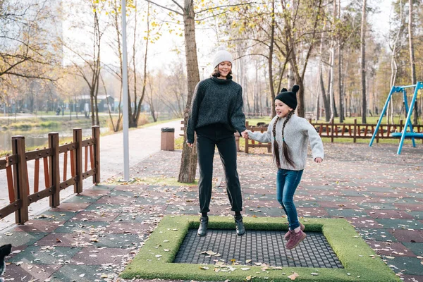 Mamá y su hija saltando juntas en el trampolín en el parque de otoño —  Fotos de Stock