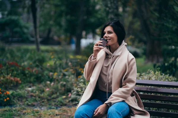 Mulher bonita sentada em um banco bebendo café desfrutando no parque — Fotografia de Stock