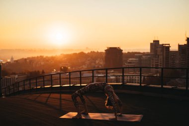 Büyük şehirde bir gökdelenin çatı üzerinde yoga yaparken kadın.