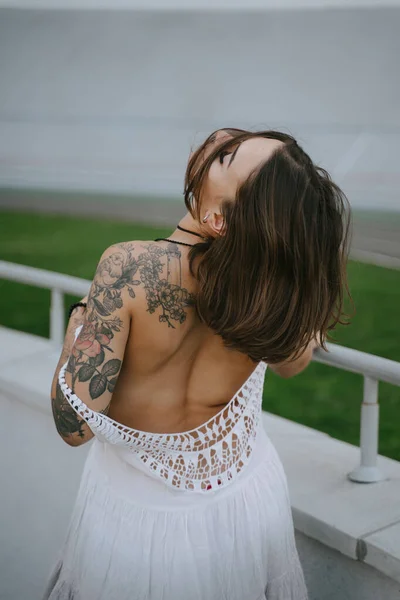 Mulher sexy esbelta mostrando suas costas bem torneadas de pé em um vestido branco, olhar por cima de seu ombro — Fotografia de Stock