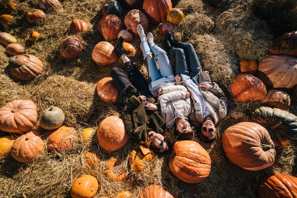 Las chicas jóvenes yacen en un pajar entre calabazas. Vista desde arriba —  Fotos de Stock