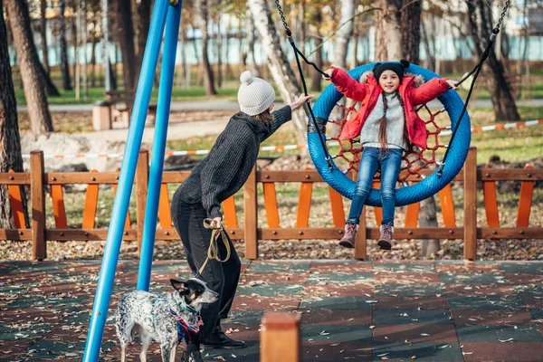 ママは秋の公園でスイングに娘をスイング — ストック写真