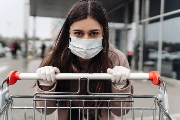 Mujer joven con máscara facial de protección contra coronavirus 2019-nCoV empujando un carrito de compras. —  Fotos de Stock