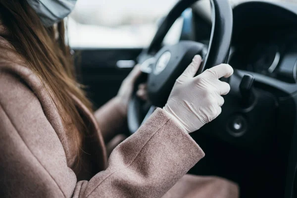 Mujer joven con una máscara y guantes conduciendo un coche. —  Fotos de Stock