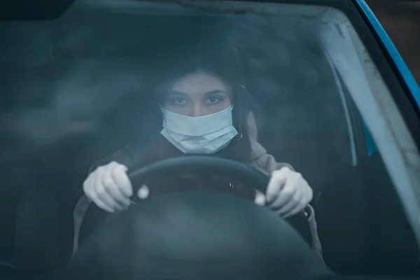 Молодая женщина в маске и перчатках за рулем автомобиля. — стоковое фото