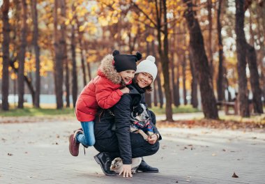 Mutlu anne ve kızı sonbahar parkında köpekle oynuyorlar.