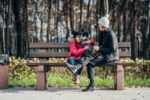 Lycklig mor och hennes dotter med hund vilar på en bänk — Stockfoto