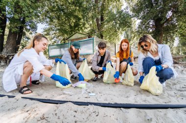 Bir grup aktivist arkadaş plajda plastik atık topluyor. Çevresel koruma.