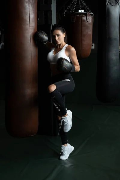 Boxoló nő, boxzsákos pózban, sötét háttérrel. Erős és független női koncepció — Stock Fotó