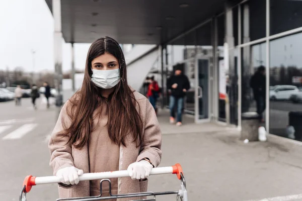 Молодая женщина в защитной маске против коронавируса 2019-nCoV толкает корзину. — стоковое фото