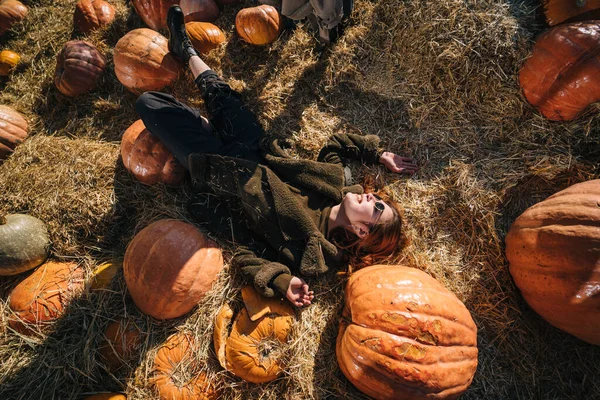 La joven se acuesta en un pajar entre calabazas. Vista desde arriba —  Fotos de Stock