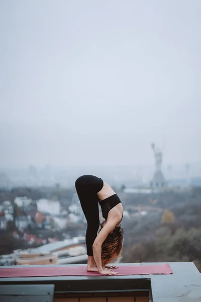 Woman practicing yoga on the mat on the roof and doing yoga exercises — Stock Photo, Image