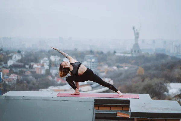 Mujer practicando yoga en la esterilla en el techo y haciendo ejercicios de yoga —  Fotos de Stock
