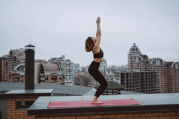 Mujer practicando yoga en la esterilla en el techo y haciendo ejercicios de yoga —  Fotos de Stock