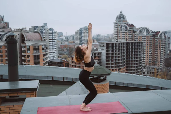 Mujer practicando yoga en la esterilla en el techo y haciendo ejercicios de yoga —  Fotos de Stock