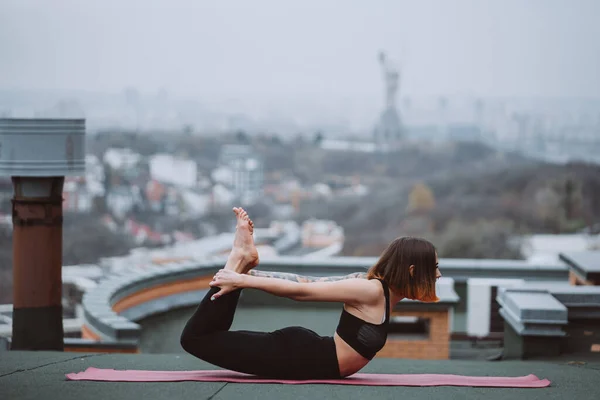 Donna che pratica yoga sul tappeto sul tetto e facendo esercizi di yoga — Foto Stock