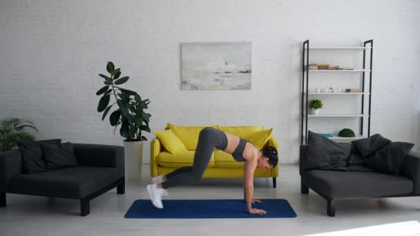 Bella giovane donna fa esercizi per l'addome sul tappeto nella stanza — Video Stock