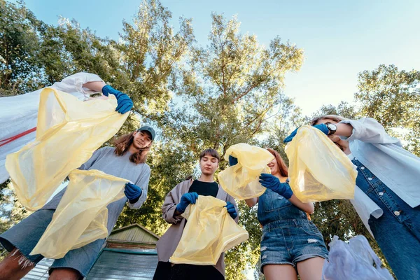 Ομάδα ακτιβιστών φίλοι πετάνε πολλά σκουπίδια σε μια τσάντα. Σκοποβολή από κάτω προς τα πάνω — Φωτογραφία Αρχείου