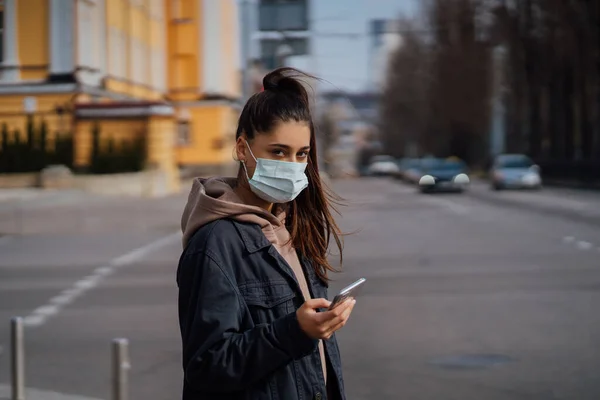 Девушка в защитной маске с помощью смартфона на открытом воздухе. COVID 19. Мировая пандемия коронавируса . — стоковое фото