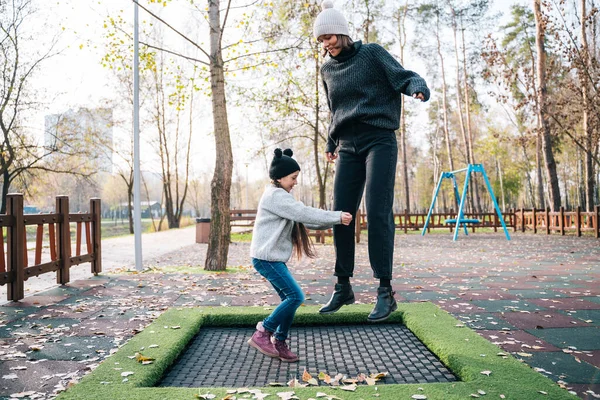Anya és lánya együtt ugrálnak a trambulinon az őszi parkban. — Stock Fotó