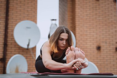 Çatıdaki minderde yoga yapan ve yoga egzersizi yapan bir kadın.